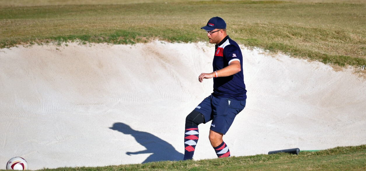 A player kicks a ball in a sand pit on the golf course.